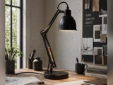 En sort, justerbar bordlampe lyser op på et arbejdsbord af træ, omgivet af bøger, skitser og tegnematerialer, med designplader og et vindue i baggrunden.