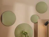 Fire runde spejle i forskellige størrelser er monteret på en beige væg; en plante og en sort lampe er delvist synlige i nederste højre hjørne.