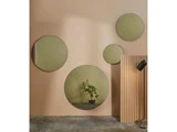 En beige væg med fire runde spejle i forskellige størrelser, en potteplante, et træpanel og en sort væglampe arrangeret i en moderne minimalistisk stil.