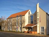 En moderne beige bygning med rødt tegltag med navnet City Hotel står ved en vej med nøgne træer og klar blå himmel i baggrunden.