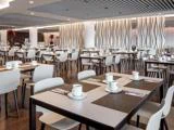 Moderne restaurant med hvide stole og borde, borddækning med kopper og underkopper og dekorative, bølgede skillevægge i baggrunden.