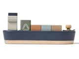 Legetøjsbåd af træ med farverige rektangulære klodser på toppen, bl.a. en med et hvidt genbrugssymbol. Båden er blå med en base af naturtræ og en lille træknap foran.