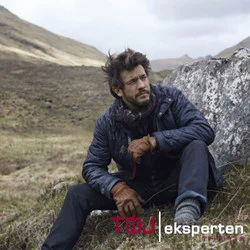 En mand i udendørstøj sidder på en klippe i et barskt, græsklædt landskab med bakker i baggrunden. Teksten Tøf eksperten er synlig i nederste højre hjørne.