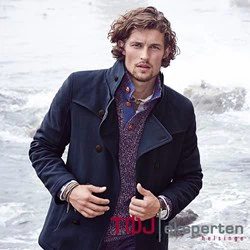 En mand med krøllet hår iført marineblå frakke og lilla sweater står ved klippekysten og kigger ind i kameraet. Ordene TDJ eksperten helsinge står i nederste højre hjørne.