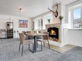 En hyggelig spisestue med pejs, hjortegevirer monteret ovenpå, moderne borde og stole, vinkøleskab, store vinduer og moderne kunstværker på væggen.