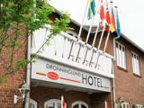 Indgangen til Dronninglund Hotel med flere flag over skiltet, knyttet til en rød murstensbygning.