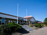 En lav, moderne bygning med et Hotel Falken-skilt og et stort HOTEL-skilt på taget, med trapper, der fører til indgangen og klar blå himmel over.
