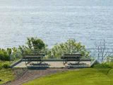 To picnicborde står på en træplatform med glasrækværk med udsigt over et roligt vandområde omgivet af grønne områder.