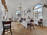 Elegant restaurantlokale med træstole, borde dækket med hvide duge og røde roser, store buede vinduer, der lukker naturligt lys ind, og moderne lysekroner.