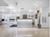 Moderne, lyst receptionsområde med hvidt skrivebord, klinkegulv, kontorstole og vægdekoration. Blå stole og borde er synlige i baggrunden.