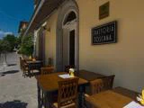 Udendørs siddeområde på et trattoria med træborde og -stole, menuer på bordene og et skilt med teksten Trattoria Toscana på en gul bygning.