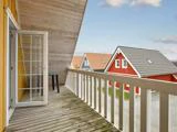Fra en træbalkon med hvidt rækværk og en åben glasdør er der udsigt til de nærliggende røde og grå huse med skrånende tage under en delvist overskyet himmel.