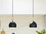 To moderne pendler med sorte skærme og træplader hænger over en køkkenbordplade med marmorbagside og lidt grønt til højre.
