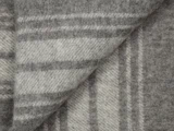 Nærbillede af et foldet, blødt, grå- og hvidstribet uldtæppe, der viser dets struktur og rektangulære mønster.