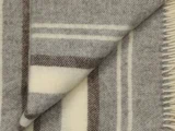 Nærbillede af et uldtæppe med beige, brune og cremefarvede striber og et foldet hjørne, der viser den bløde tekstur og frynsekanten.