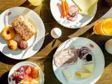 Morgenmad med brød, kager, ost, pålæg, skiveskårne grøntsager, frugt, vindruer og glas med appelsinjuice arrangeret på et træbord.