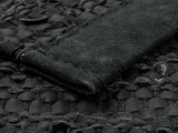 Nærbillede af et struktureret sort læder- og ruskindsmateriale med synlige syninger og vævede mønsterdetaljer.