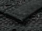 Nærbillede af et struktureret sort læder- og ruskindsmateriale med synlige syninger og vævede mønsterdetaljer.