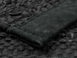 Nærbillede af et tekstureret sort læder- og ruskindsmateriale, der viser detaljerede syninger og et vævet mønster.
