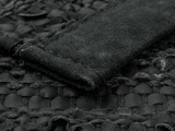 Nærbillede af et struktureret sort vævet stof med en hævet ruskindsstribe syet på tværs af overfladen.