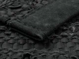 Nærbillede af et struktureret sort vævet stof med en hævet ruskindsstribe syet på tværs af overfladen.