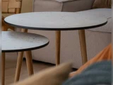 To runde borde med lysegrå plader og træben er placeret foran en beige sofa i en hyggelig stue.