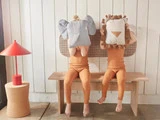 To børn i matchende orange pyjamas sidder på en bænk og holder hver en stor dyrepude - en elefant og en løve - over hovedet, mens de leger, at de skjuler deres ansigter.