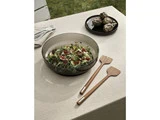 En skål med frisk salat med figner og grønt står på en beige dug, ledsaget af salatbestik i træ og en tallerken med to artiskokker i baggrunden.