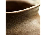 Nærbillede af den strukturerede, afrundede kant og hals på en brun keramikkrukke, der viser den ru, matte overflade og naturlige ufuldkommenheder.