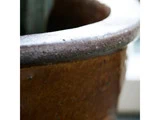 Nærbillede af den strukturerede kant og oversiden af en brun keramikpotte med blødt naturligt lys og sløret baggrund.
