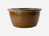 En rund, brun keramikpotte med en bred åbning og en let hævet kant på en almindelig lysegrå baggrund.