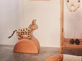 En plettet leopard iført en lille festhat står på en buet træklods ved siden af en kurvestol i et svagt oplyst rum.