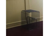 Et par minimalistiske sideborde i sort metal med åbne, trådformede design, placeret mod en beige væg og på et mørkt gulvtæppe.