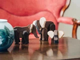 Tre elefantfigurer af træ står på et træbord med en blå og hvid vase og en rød polstret stol i baggrunden.
