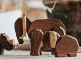 Tre udskårne elefantfigurer af træ i forskellige størrelser er anbragt på en flade med en sløret baggrund.