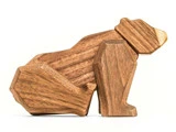 En træskulptur af en bjørn i siddende stilling, udformet med geometriske former og glatte kanter mod en hvid baggrund.