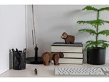 Et minimalistisk skrivebord med bøger, en lampe, en potteplante, kuglepenne i en holder, bjørnefigurer i træ, en kuglepen og et hvidt tastatur.
