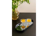 To cocktails med appelsinskiver står på en spejlbakke på et mørkt bord ved siden af en glasvase med grønt løv og små hvide blomster.