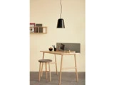 Minimalistisk arbejdsplads med skrivebord og skammel i træ, en lille hylde med bøger, en skillevæg med noter og en sort pendellampe over.