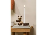 En panda-figur i træ står ved siden af et højt, tændt hvidt lys i en marmorholder, begge placeret på en stak bøger på et træbord.