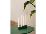 Fire tændte hvide stearinlys i en moderne grøn holder står på et rundt grønt bord med en bladplante og en del af en beige stol i baggrunden.