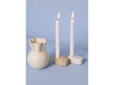 En cremefarvet vase og to tændte hvide lys i stenholdere står på en lyseblå baggrund.