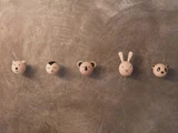 Fem runde vægkroge i træ formet som dyreansigter - bjørn, fugl, koala, kanin og panda - monteret på en struktureret grå væg.