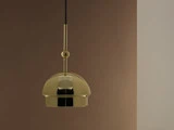 En moderne guldpendel hænger foran en brun og beige tofarvet væg.