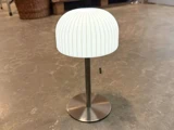 En moderne bordlampe med en hvid, ribbet, kuppelformet lampeskærm, metalfod og trækæde, placeret på et struktureret stengulv.