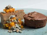 En tallerken med et stykke kage toppet med mango i tern og kerner, ved siden af en portion chokolademousse på et blåt keramikfad.