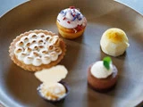 En brun tallerken med fem forskellige desserter i mundrette størrelser, bl.a. en tærte med ristet marengs, en mini-cupcake med creme og en rund hvid trøffel.