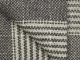 Nærbillede af foldet stof med et vævet mønster i sort, hvid og grå med vandrette og lodrette striber og en struktureret overflade.