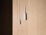 To minimalistiske hvide pendler hænger op ad en lys trævæg, hvor sollyset kaster en skygge på venstre side.