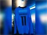 En lyseblå sportstrøje med lange ærmer, der hænger på en bøjle, med navnet MAHMOUD og nummeret 11 på ryggen.
